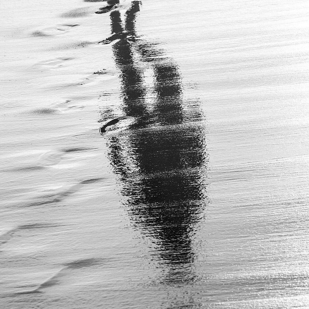 Reflection of a person walking on wet sand, symbolizing the afterlife and spiritual journey.