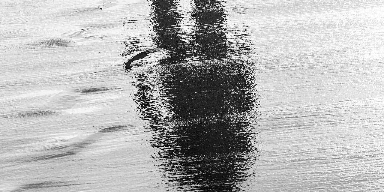 Reflection of a person walking on wet sand, symbolizing the afterlife and spiritual journey.