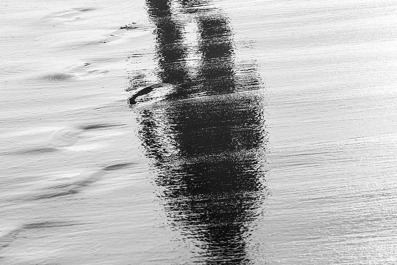 Reflection of a person walking on wet sand, symbolizing the afterlife and spiritual journey.