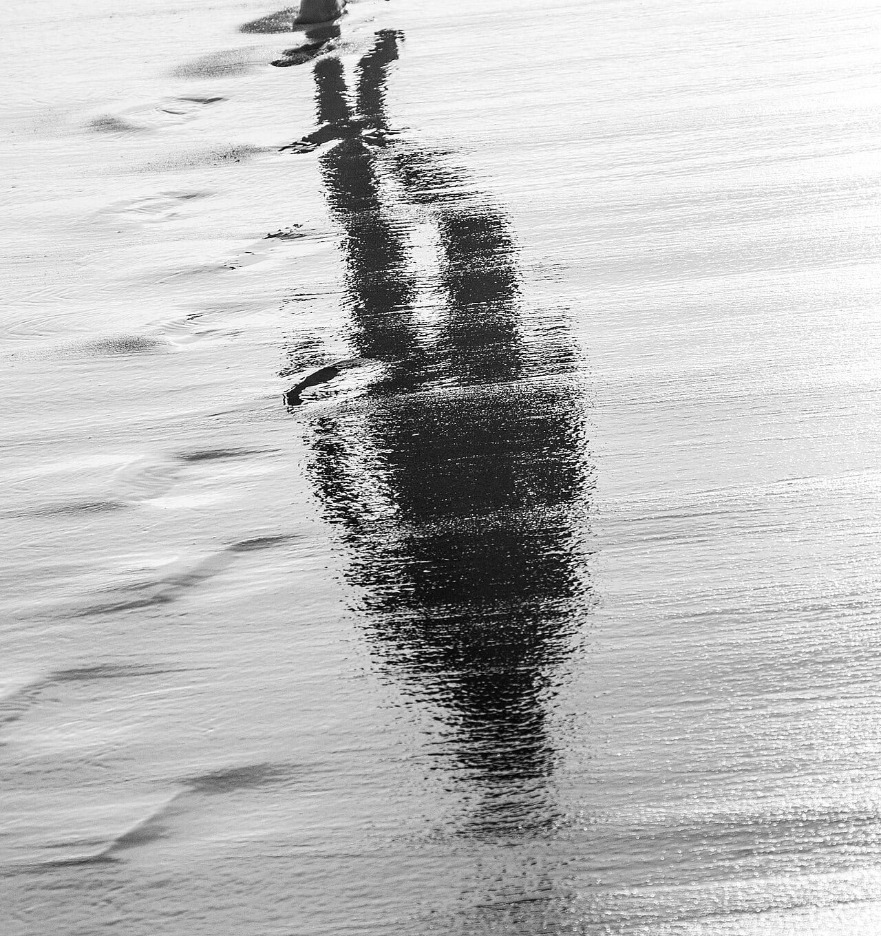 Reflection of a person walking on wet sand, symbolizing the afterlife and spiritual journey.
