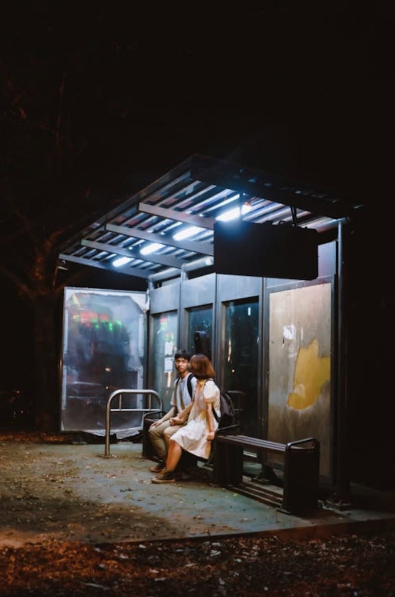 Bus stop shelter with seating, illuminated at night, featuring two women waiting.
