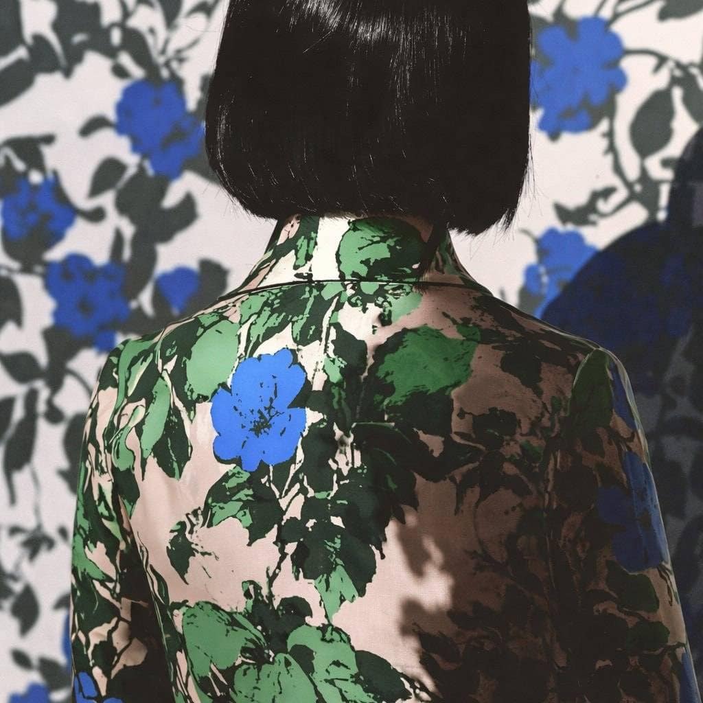 Woman with short black hair wearing a floral patterned jacket against a matching background.
