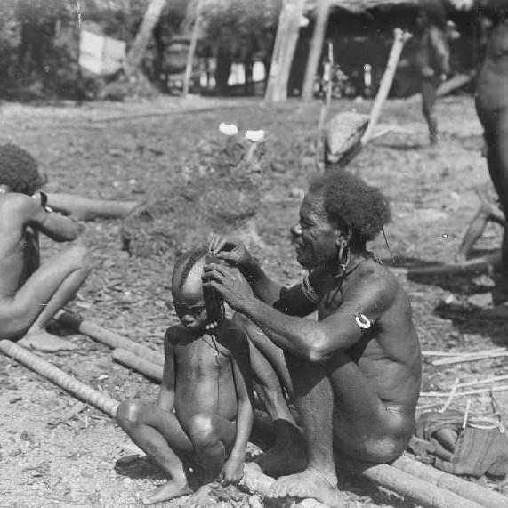 Indigenous family engaging in cultural grooming and bonding outdoors.