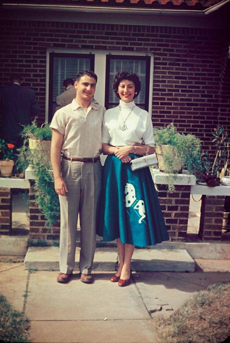 Two people celebrating outdoors with plants and brick background.