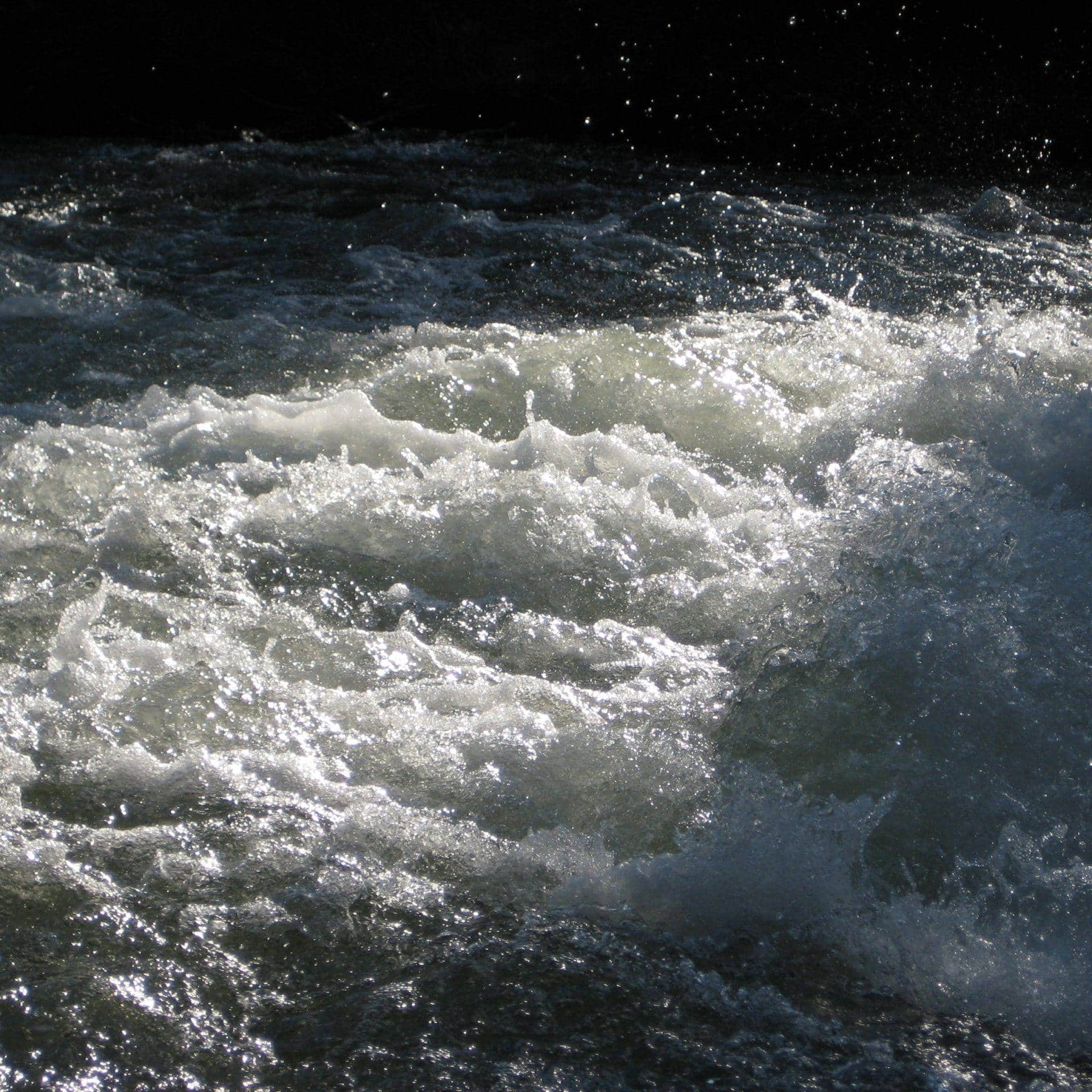 Fast-moving river with white water rapids and dark surrounding rocks.