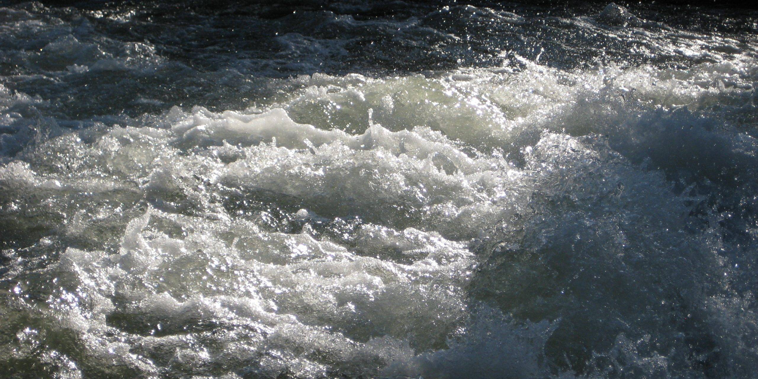 Fast-moving river with white water rapids and dark surrounding rocks.