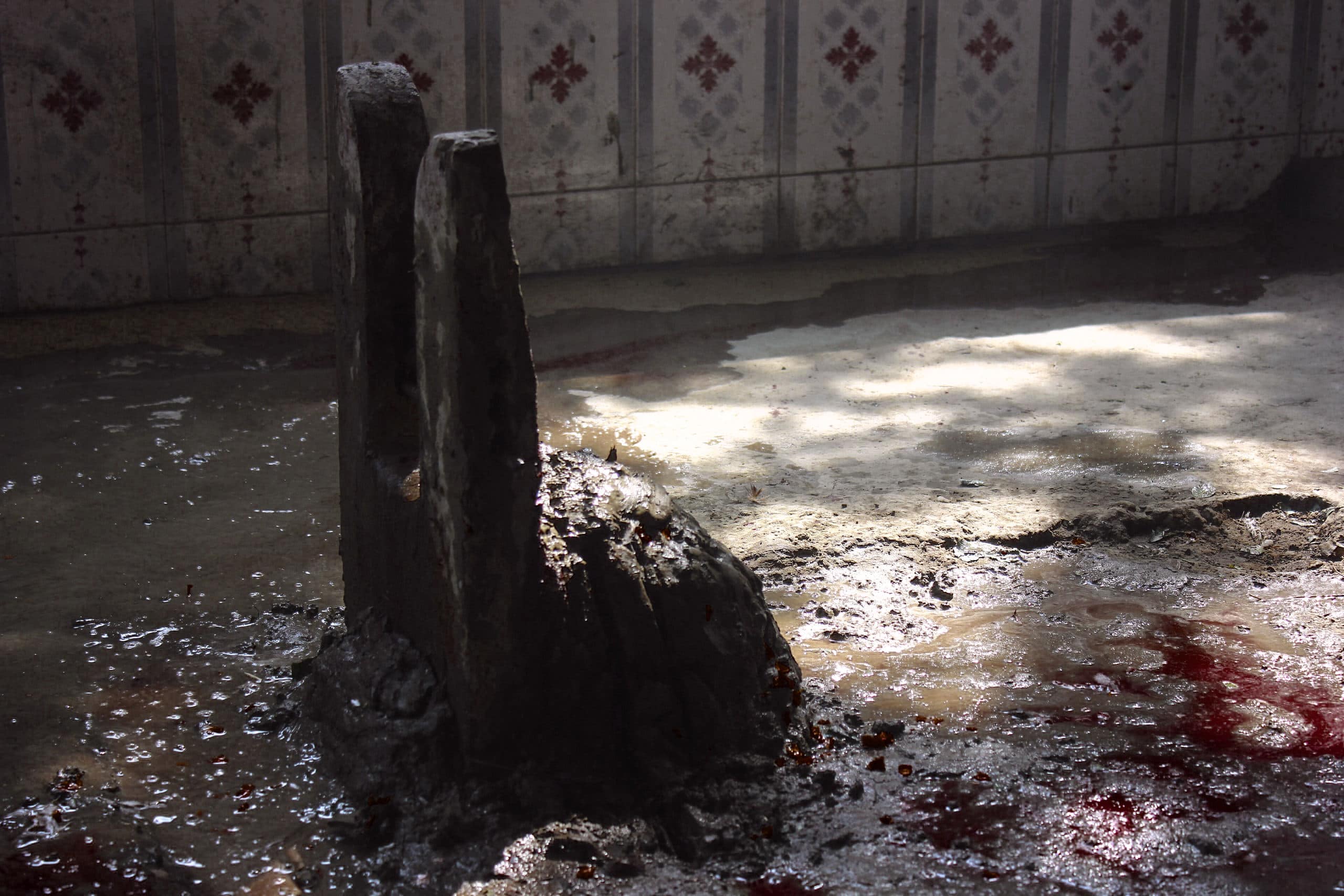 Ancient ritual stone with dark, weathered surface on a tiled floor, surrounded by water and blood st.