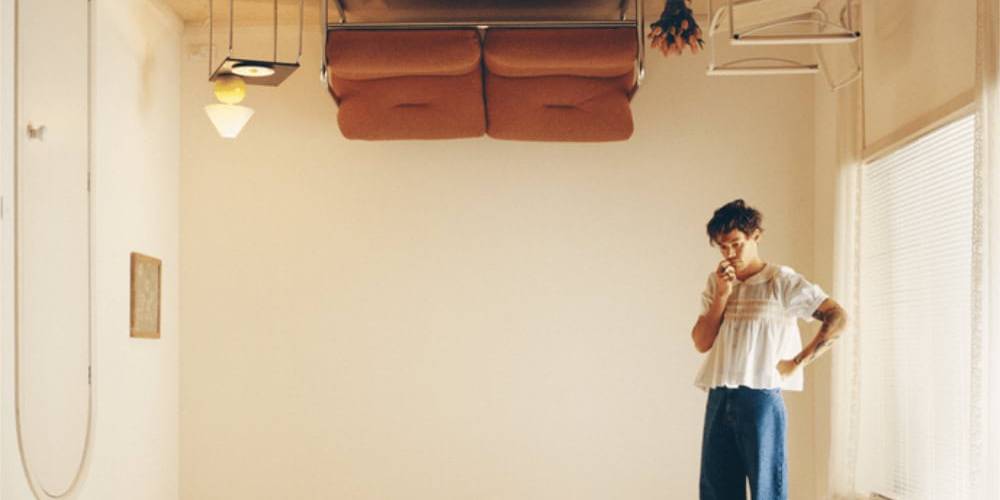 Upside-down furniture in a minimalist room with a woman pondering, creating a surreal, thought-provo.