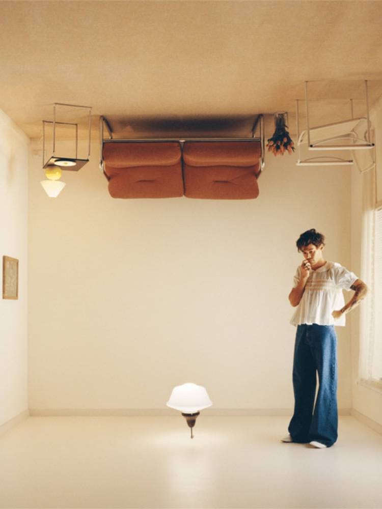 Upside-down furniture in a minimalist room with a woman pondering, creating a surreal, thought-provo.