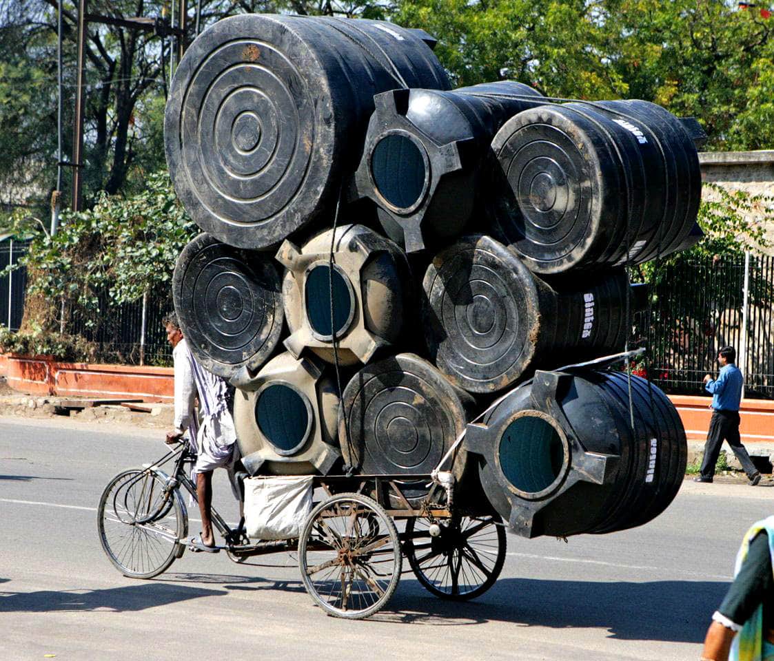 Overloaded cart carrying oversized tires and drums, illustrating burden and imbalance in the context.