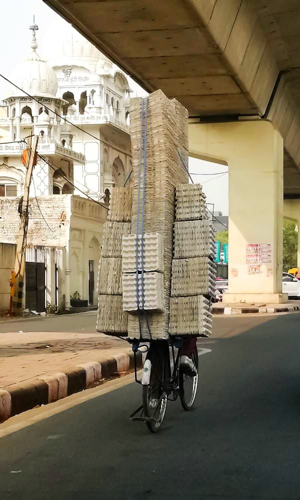 Cyclist transporting large brick stacks under an overpass in an urban setting.