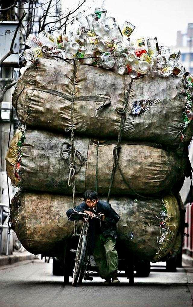 Garbage truck overloaded with trash and aluminum cans in an urban setting.