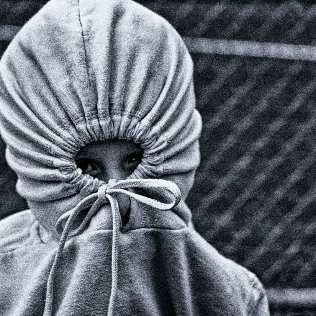 Person with hoodie covering face, symbolizing shame and concealment.