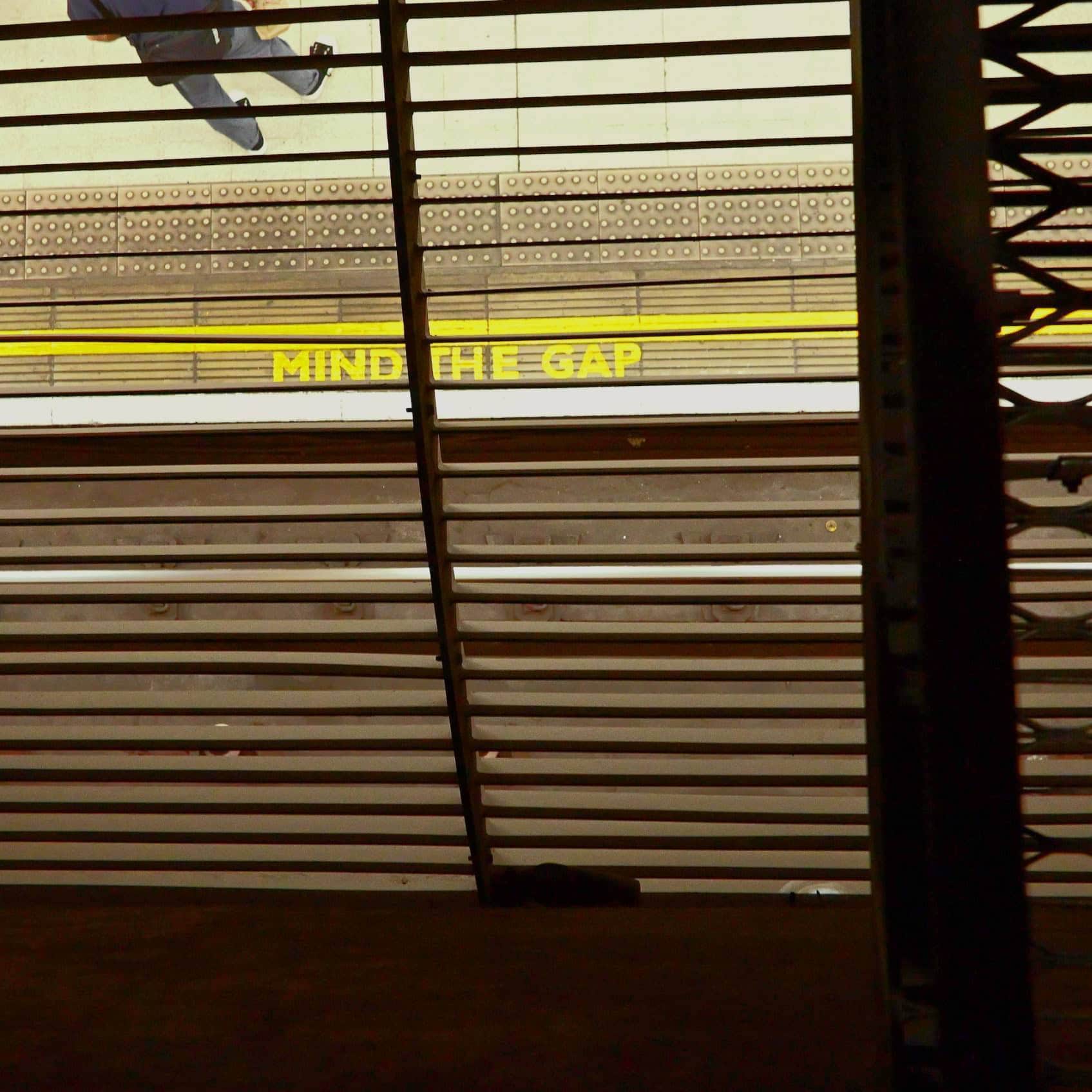 Yellow 'Mind the Gap' sign on train platform with safety lines.
