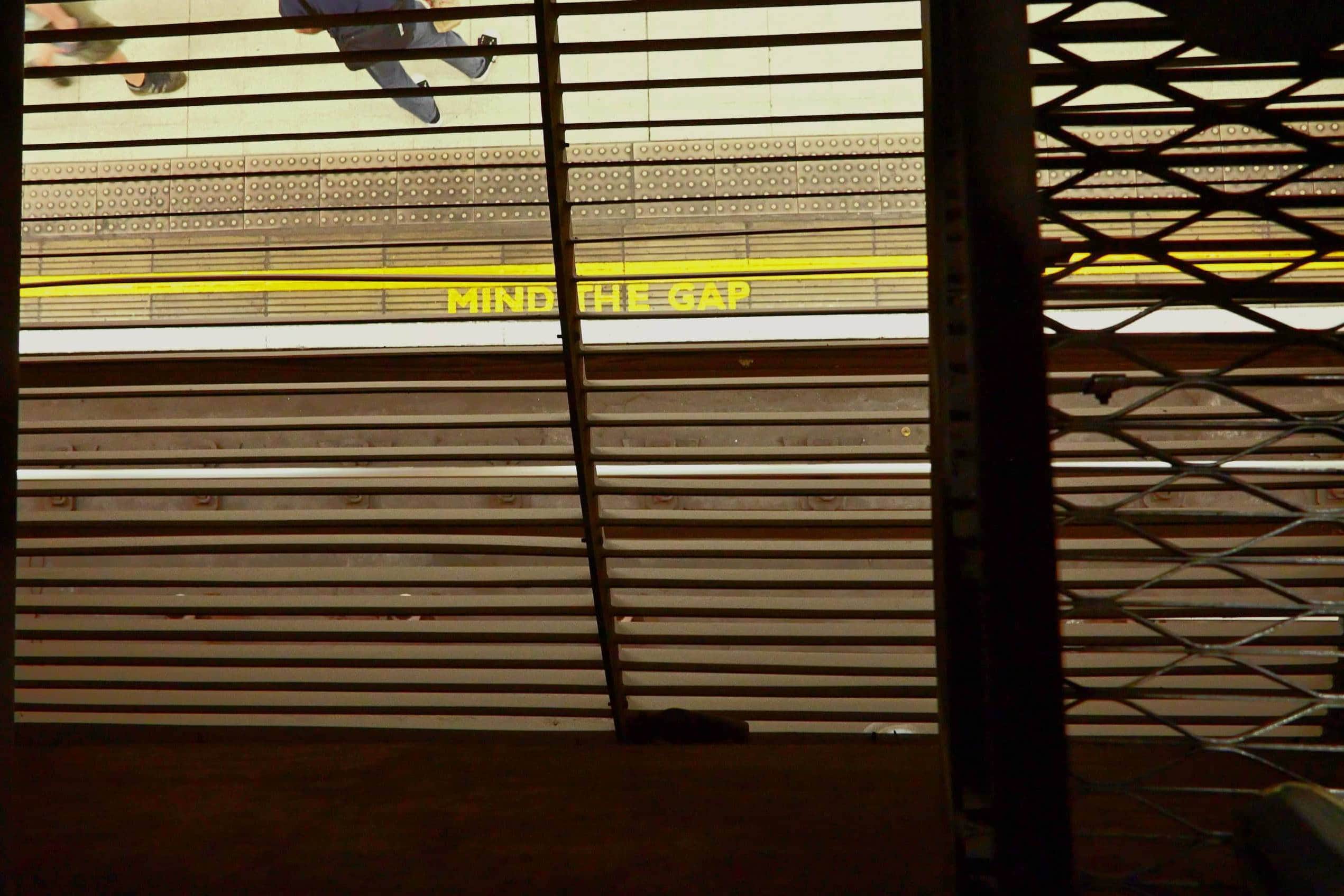 Yellow 'Mind the Gap' sign on train platform with safety lines.