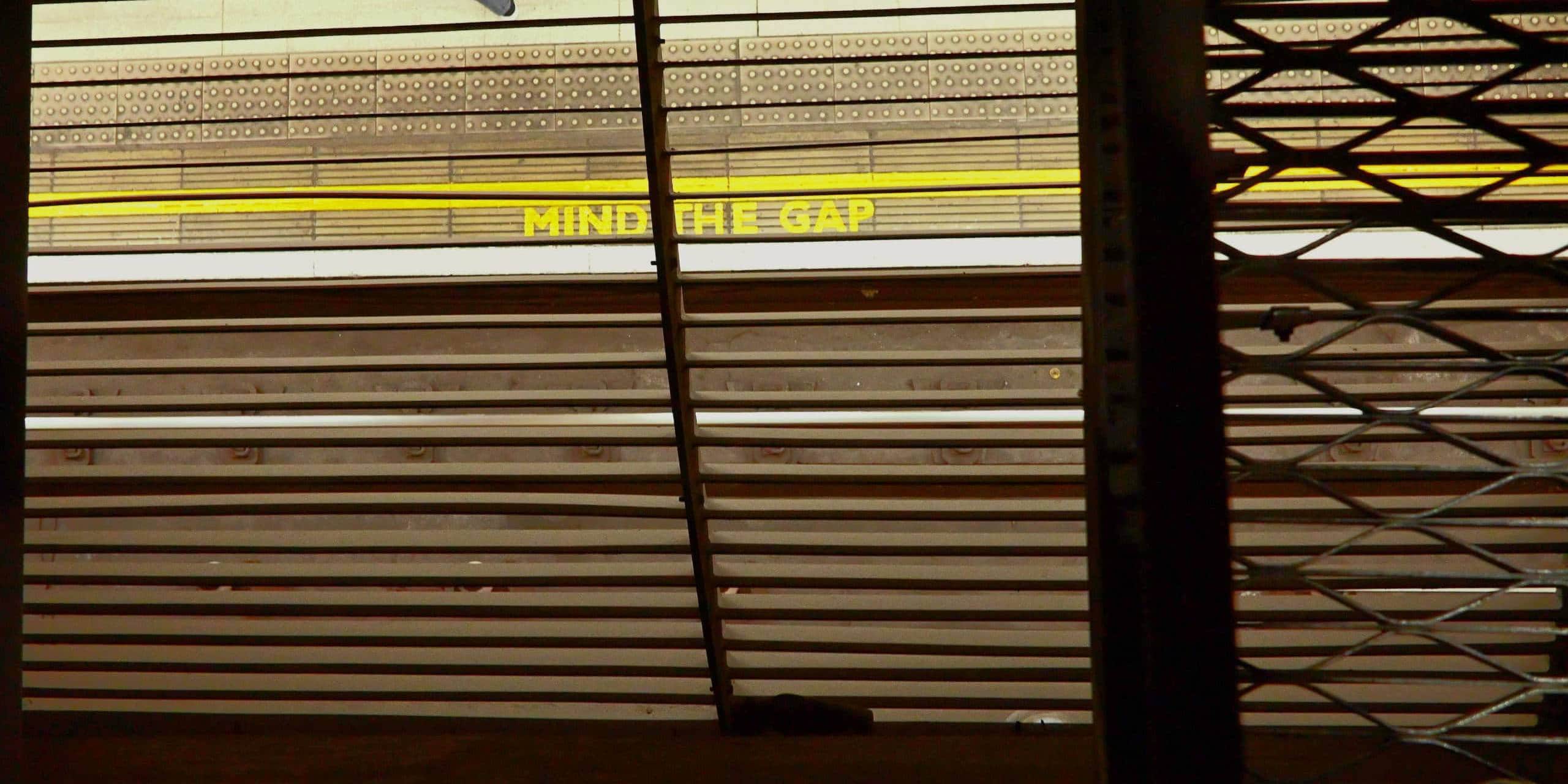 Yellow 'Mind the Gap' sign on train platform with safety lines.