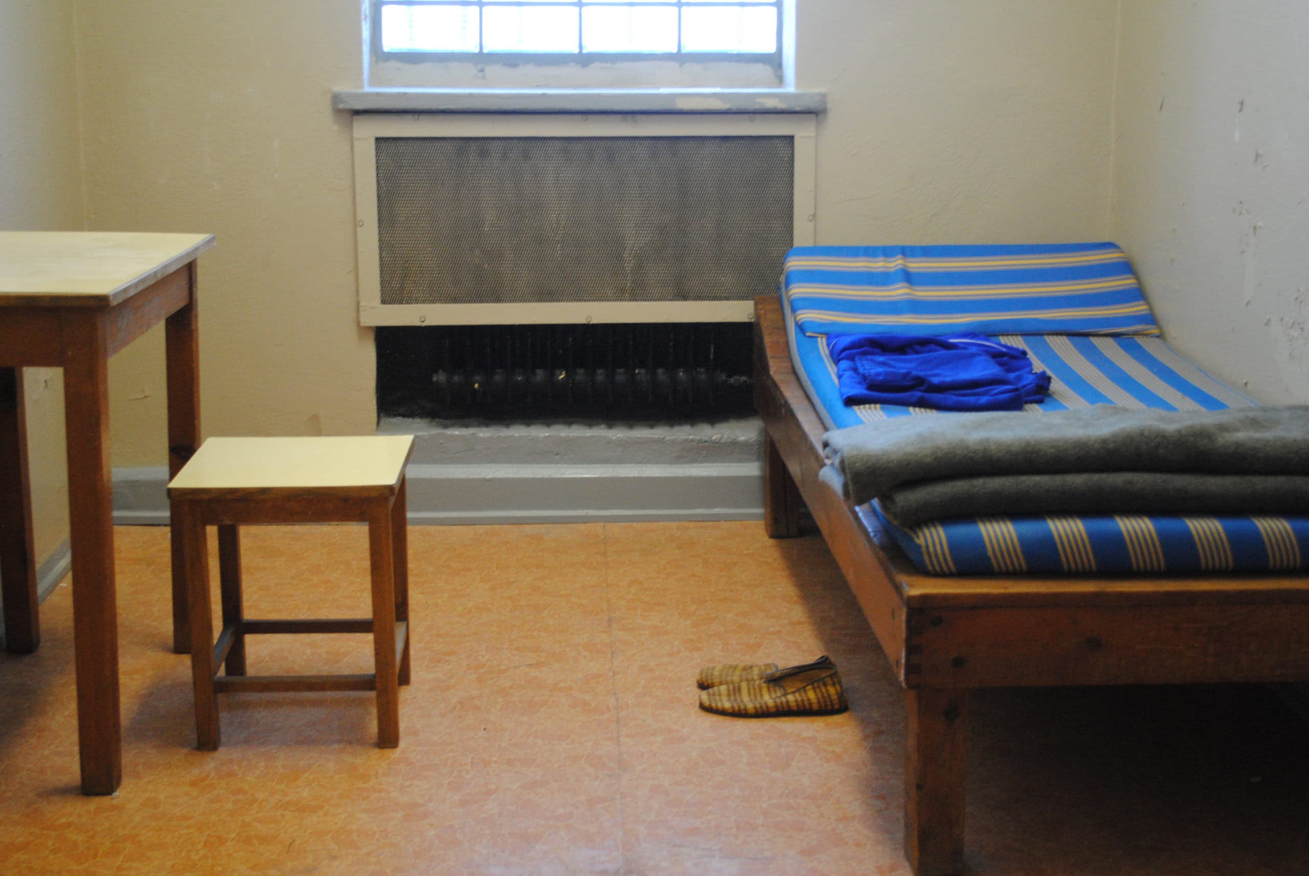 Simple room with bed, small table, stool, and window in a basic setting.