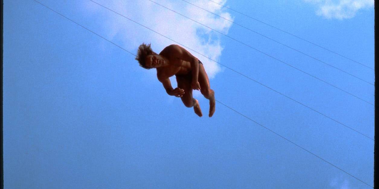Aerial performer midair during a stunt against a blue sky with clouds.