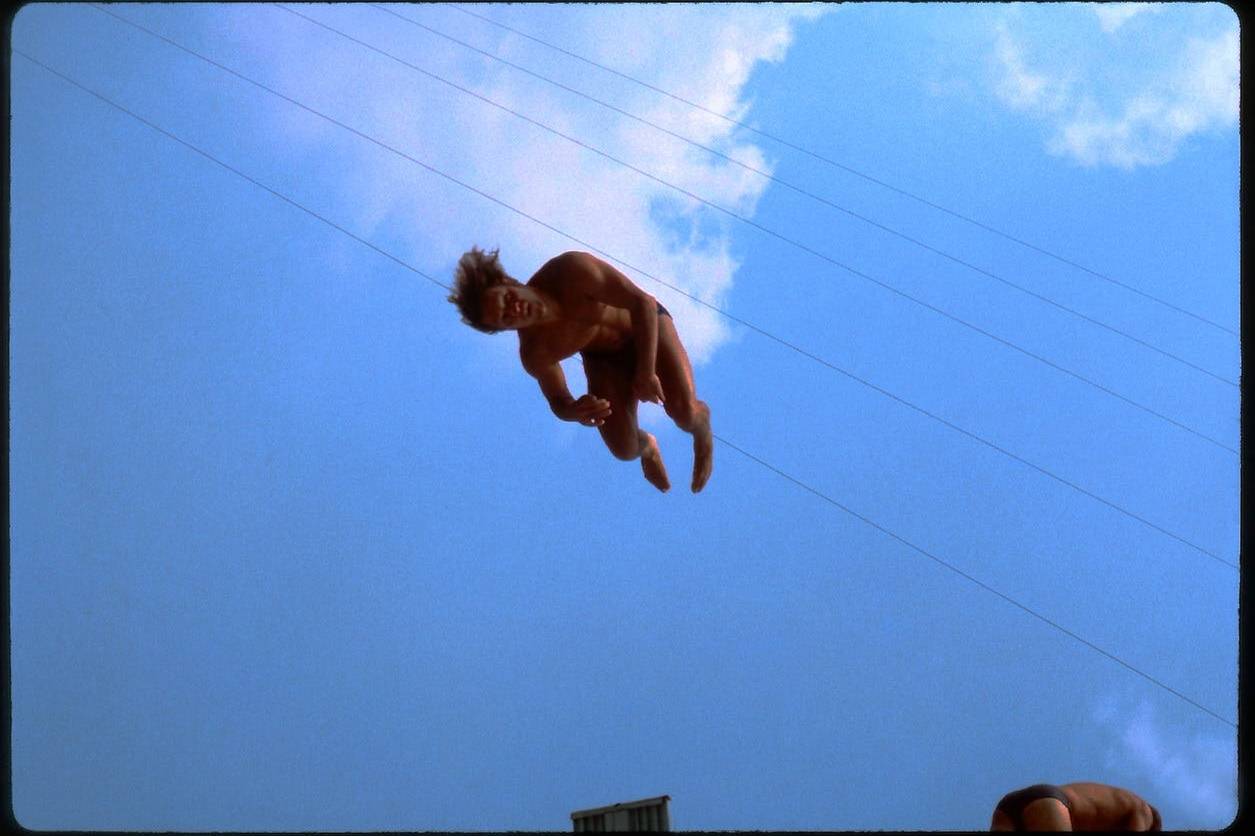 Aerial performer midair during a stunt against a blue sky with clouds.