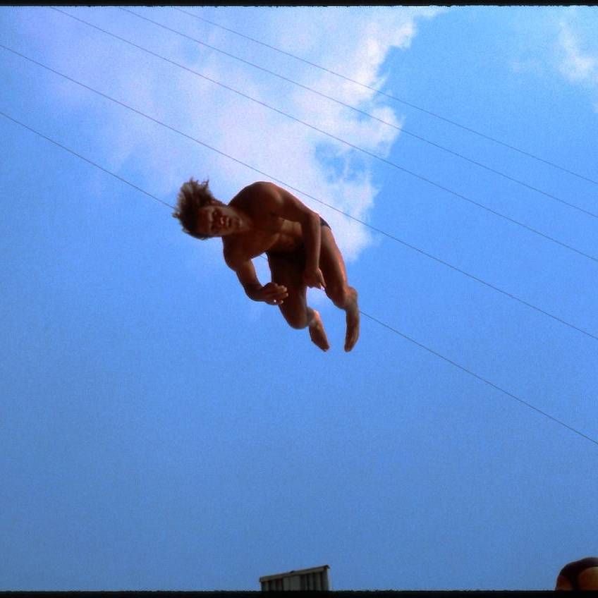 Aerial performer midair during a stunt against a blue sky with clouds.