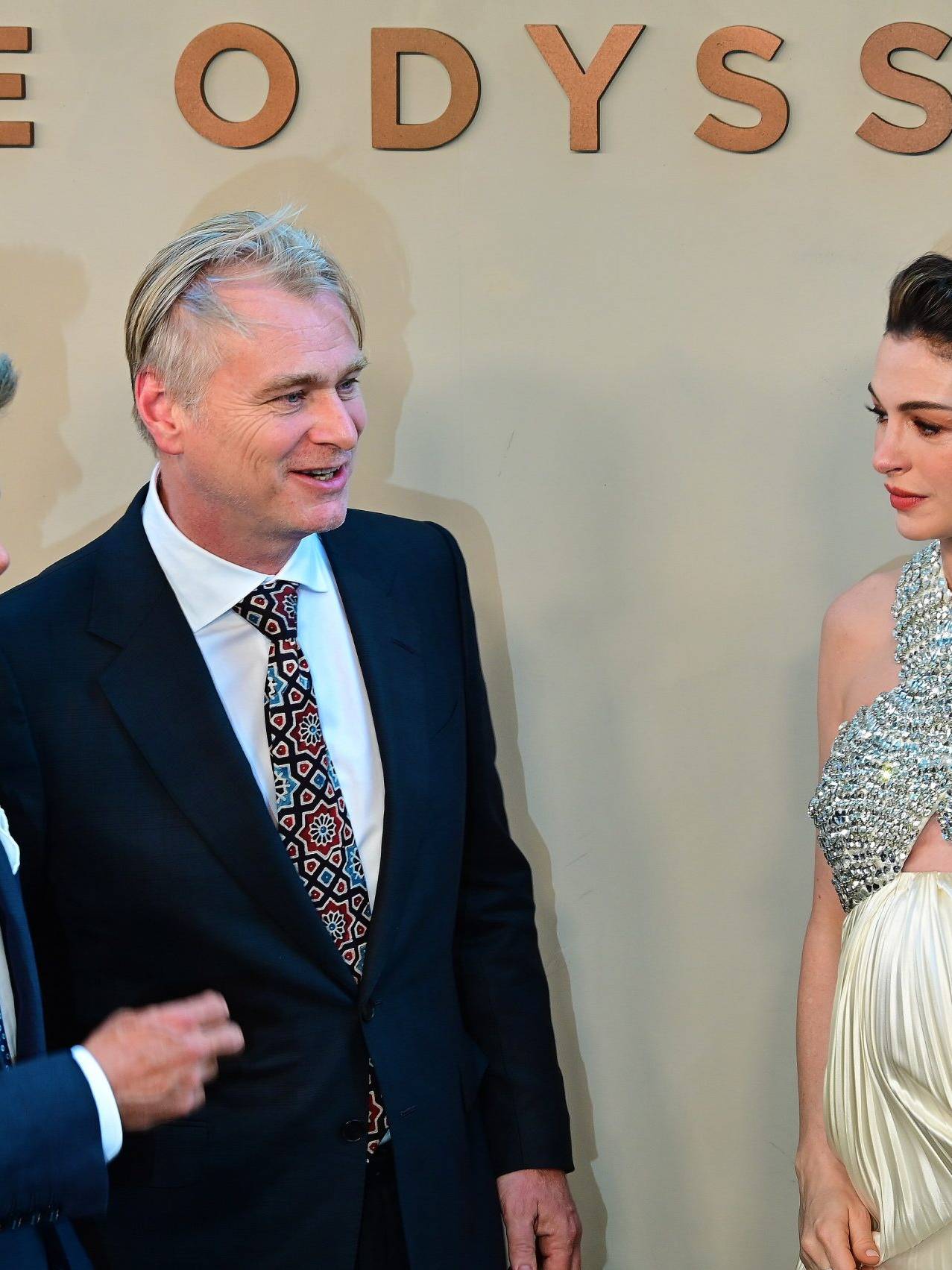 Three people in formal attire at The Odyssey event, engaging in conversation.
