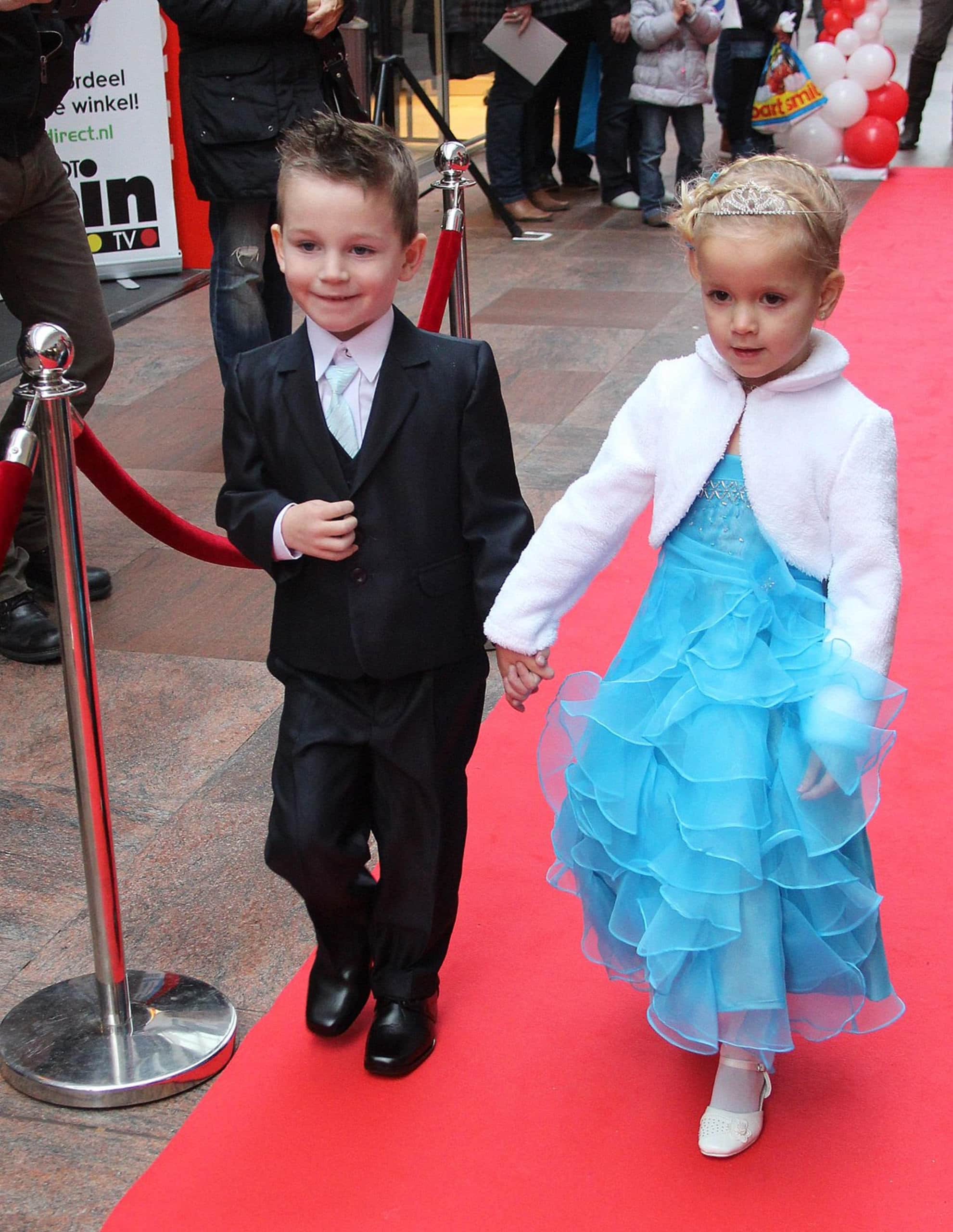 Young boy and girl holding hands on red carpet at a public event.