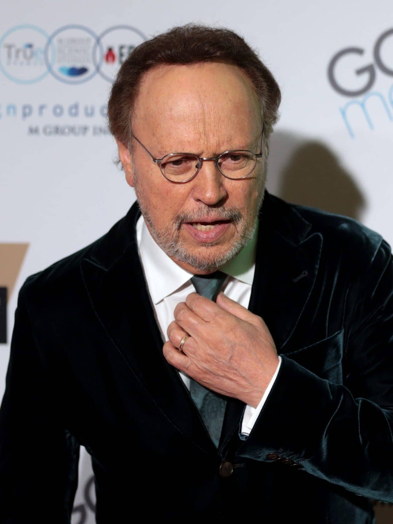 Celebrity at GRAINOFGOLD event, wearing black velvet suit and glasses.