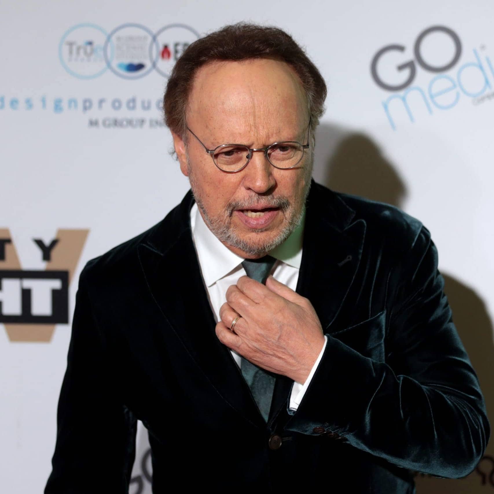 Celebrity at GRAINOFGOLD event, wearing black velvet suit and glasses.