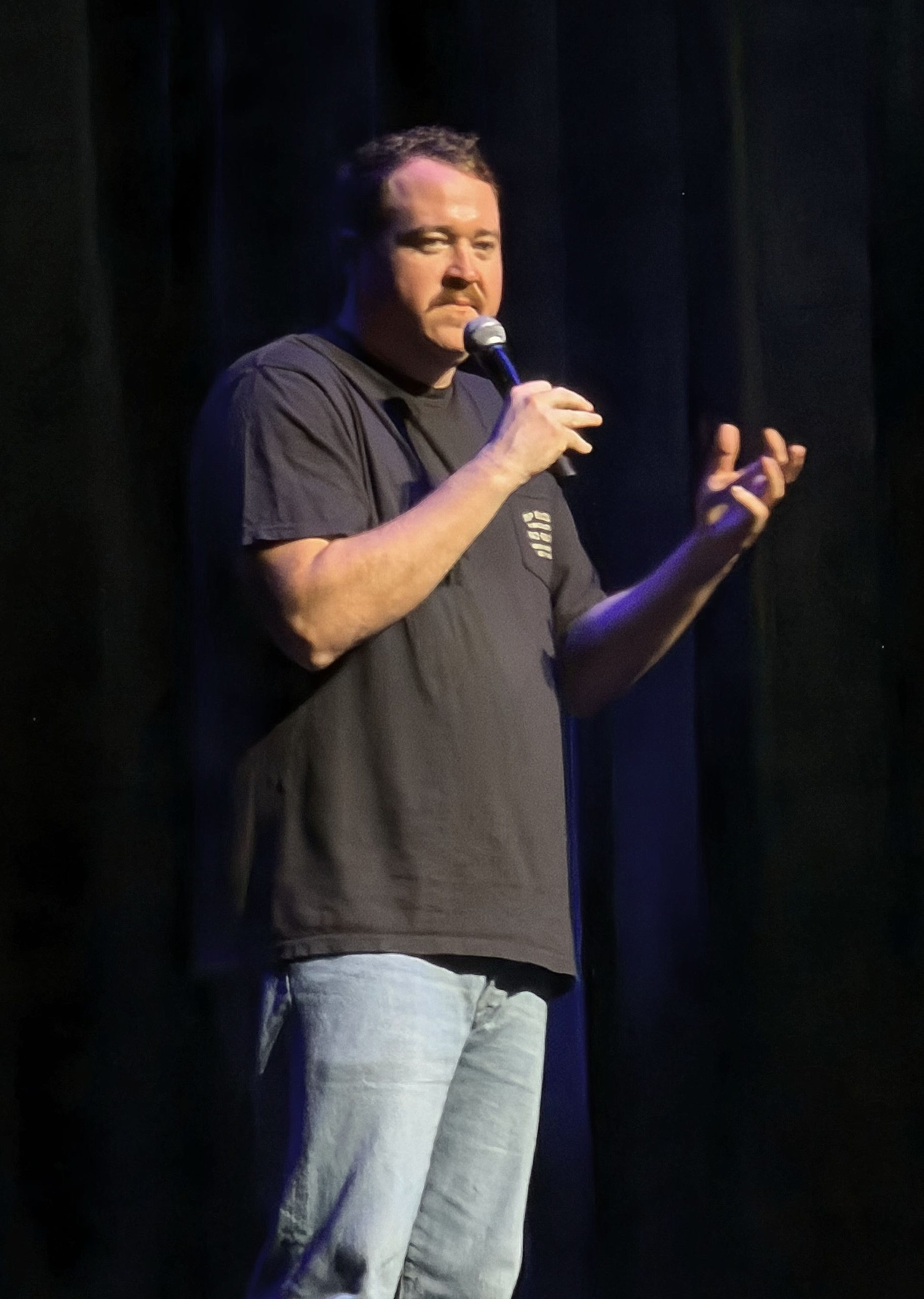 Comedian performing stand-up comedy on stage with microphone.